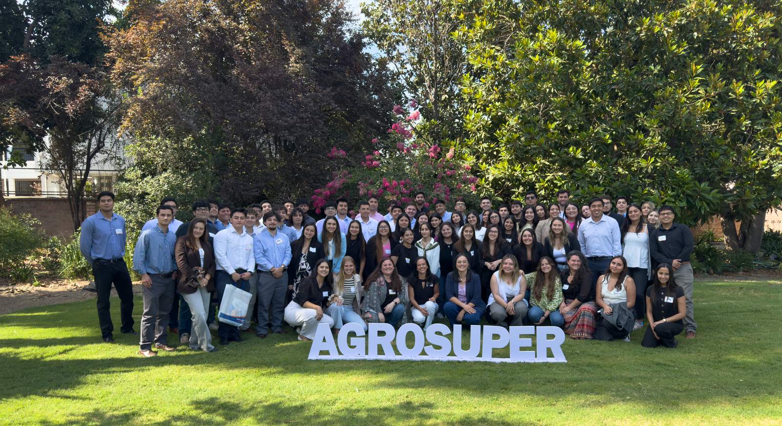 Generación de practicantes de Agrosuper reunida en un jardín junto a letras gigantes con el nombre de la empresa